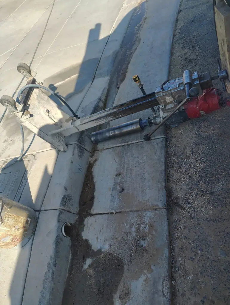 Curb coring machine drilling into concrete for pavement repair.
