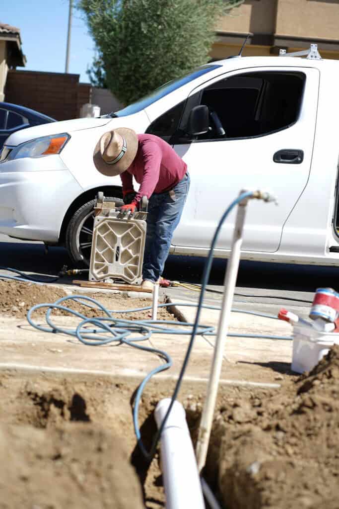 Technician performing curb core drilling with specialized equipment near a white vehicle.